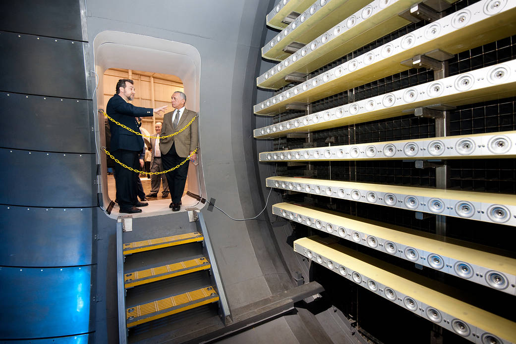 NASA Adminstrator Bolden and another man look inside an engine icing test room lined with large horizontal spray bars 