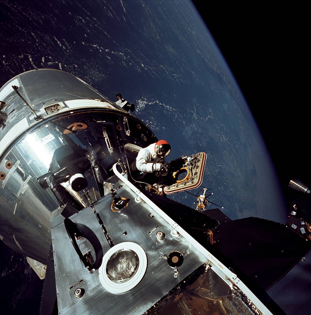 Apollo 9 astronaut Dave Scott stands in the open hatch of the Command Module, nicknamed "Gumdrop," docked to the Lunar Module "Spider" in Earth orbit.