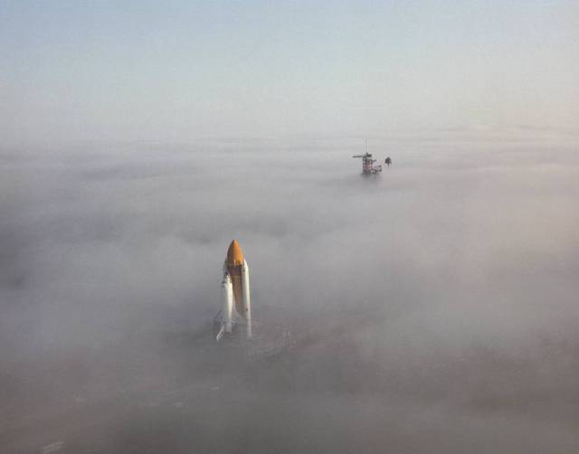 Space shuttle Challenger presents a surrealistic impression as it moves through the fog on its way out the 3.5-mile crawlerway toward Launch Pad 39A. 