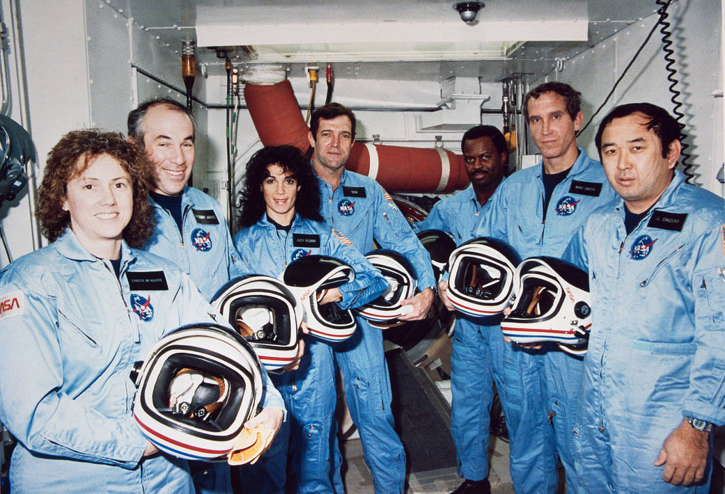 STS-51L crewmembers photographed in flight suits with helmets during a break in astronaut training.