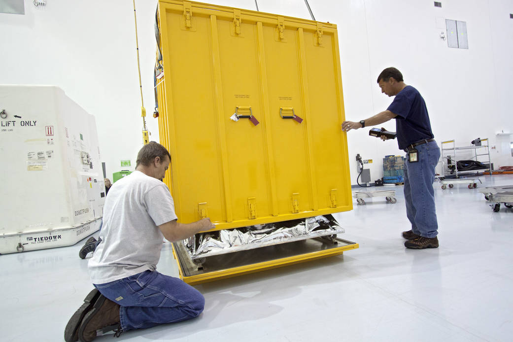Technicians lower the cover of a shipping container that will enclose the orbital replacement unit for the space station's main 