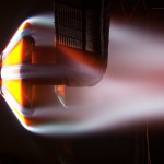 This image is from the Interactive Heating Facility ArcJet and shows the flow of extremely heated air exiting the 21-inch diameter nozzle from the left, causing a bow shock to form in front of the ADEPT test article.
