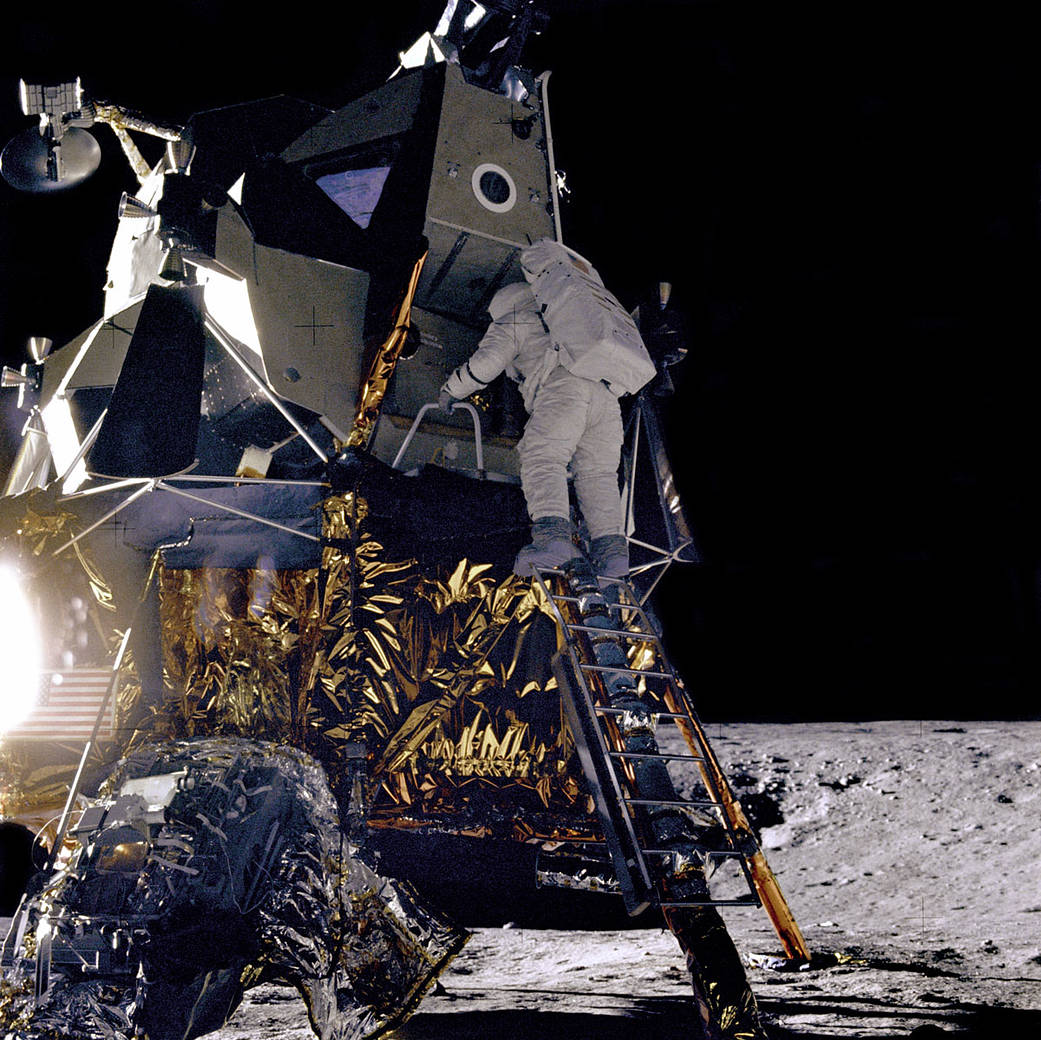 Astronaut in spacesuit climbing down from lunar module on surface of moon