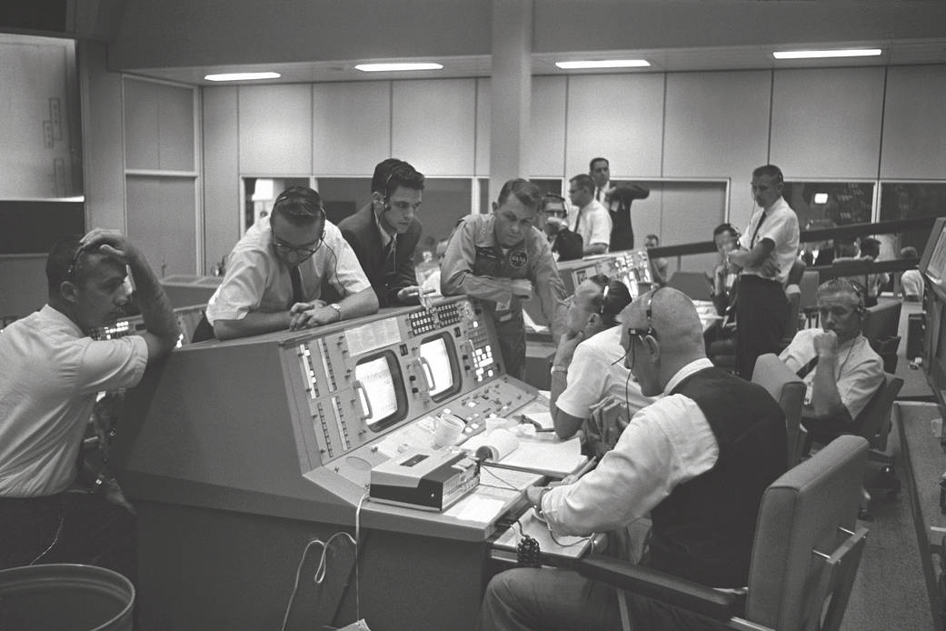 Console at Mission Control Center with flight directors seated