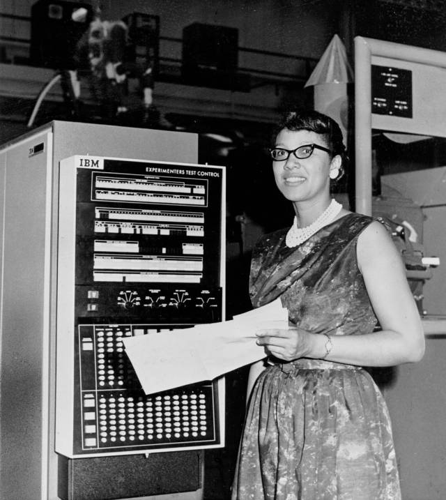Melba Roy standing next to machine with cards