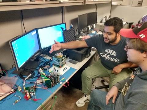 ARKSAT-1 team members Samuel Cano (left) and Charles Smith perform final checkout tests on the ARKSAT-1 flight model, with its electronics stack engineering model also shown.