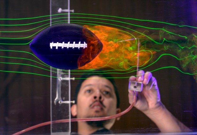 man standing near football in a water chamber with lasers and smoke around football