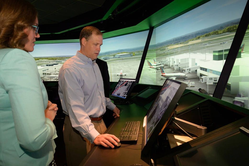 Two people participating in an air traffic control interface demonstration, with out the window tower view in background