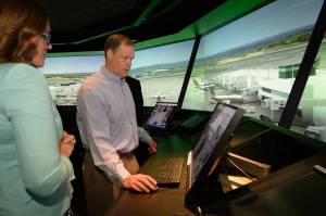 Two people participating in an air traffic control interface demonstration, with out the window tower view in background