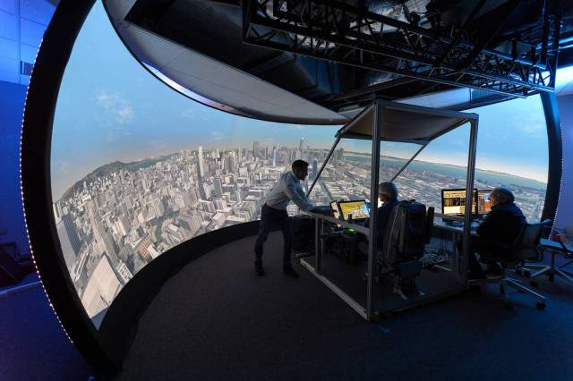 The people observe a large curved screen showing out the window views of San Francisco.