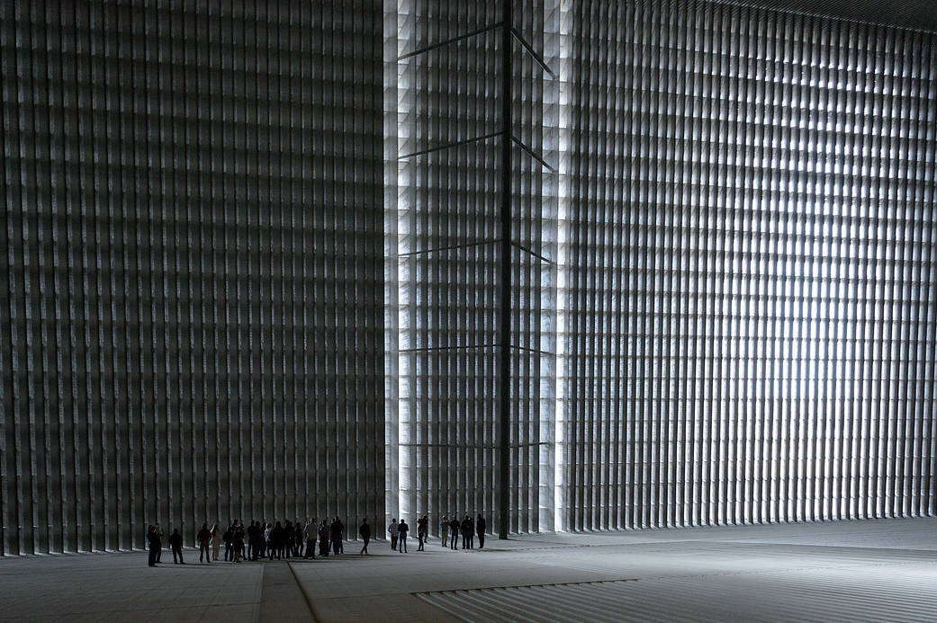 Tiny figures stand at the base of a tall grid-like wall.