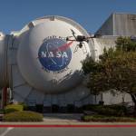 A quadcopter drone flies in front of the exterior of a wind tunnel bearing the NASA logo.