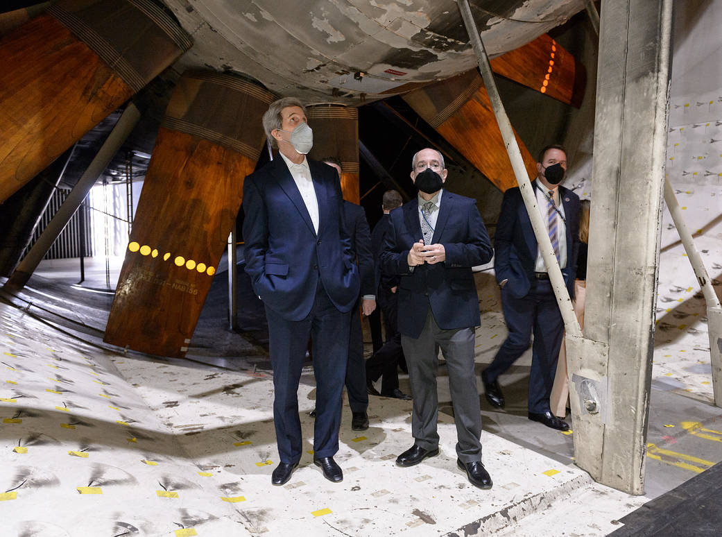 Two men in suits stand in front of the blades of an enormous fan