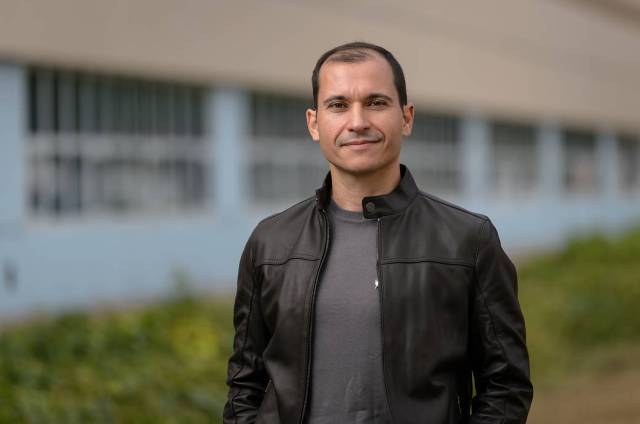 Ivan Perez Dominguez stands in front of a building with a slight smile. He is wearing a grey shirt and a leather jacket. 