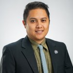Portrait of Kyle Kabasares in an army green colored shirt, blue tie and a dark grey blazer