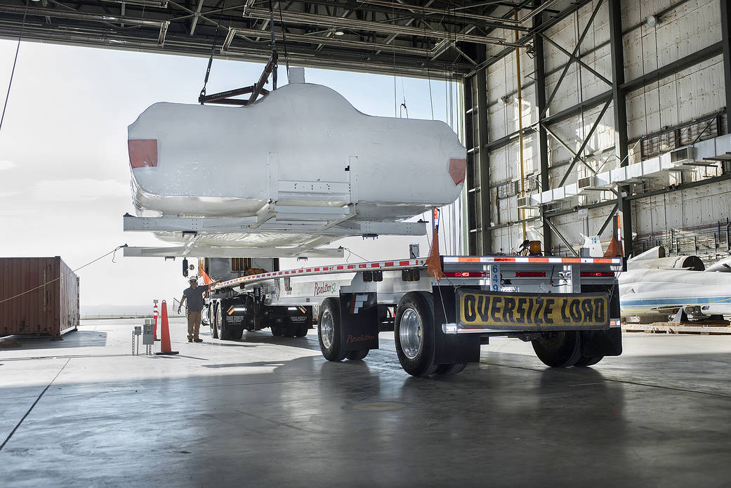 SNC Dream Chaser is lifted on to a truck in NASA Armstrong’s historic space shuttle hangar.