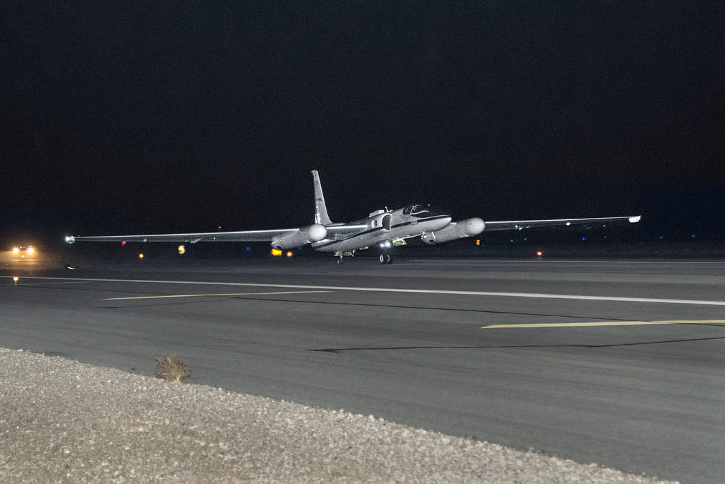  An ER-2 plane, small and thin with long white wings, takes off from a black tarmac against the night sky.
