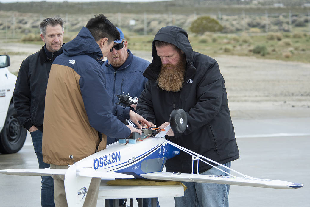 Eric Becker watches as Nathan Sam, Robert “Red” Jensen and Justin Hall attach a Prandtl-M aircraft onto the Carbon Cub.