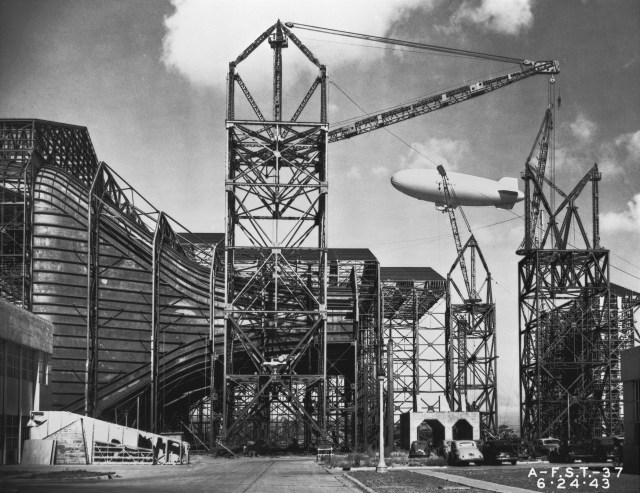 Construction of the Ames Full-Scale 440-by-80-foot wind tunnel. Side view of entrance cone, blimp in background.