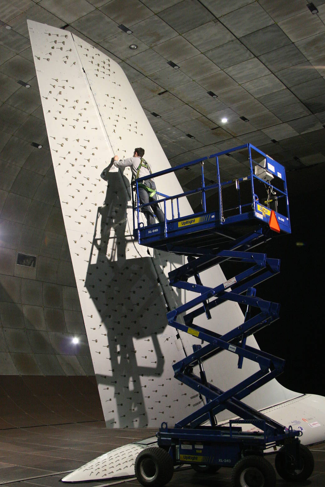A man standing on a blue lift placing tiny jets called sweeping jet actuators on the full-sized tail from a 757 commercial aircraft.