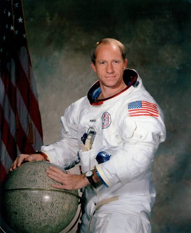 Astronaut Al Worden in white spacesuit posing with a globe