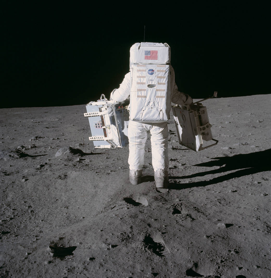 Buzz Aldrin in spacesuit holding experiment packs walking on lunar surface