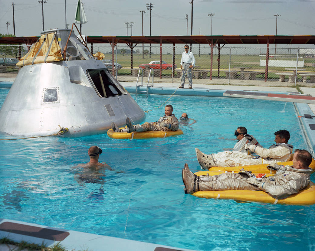  In the water at right are astronauts Ed White and Roger Chaffee (foreground). In raft near the spacecraft is astronaut Gus Grissom.