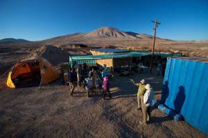 The ARADS base camp in the Atacama Desert. There are tents, the rover, and scientists talking, with mountains behind them.
