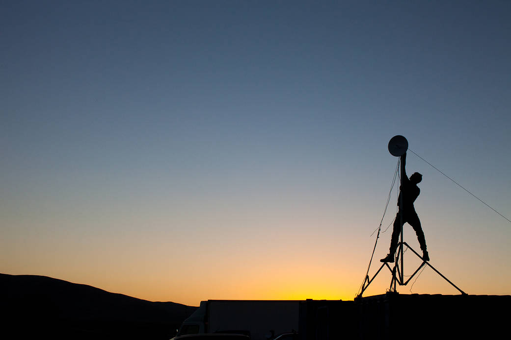 An ARADS team member is seen in silhouette setting up a communications satellite dish in the Atacama Desert.