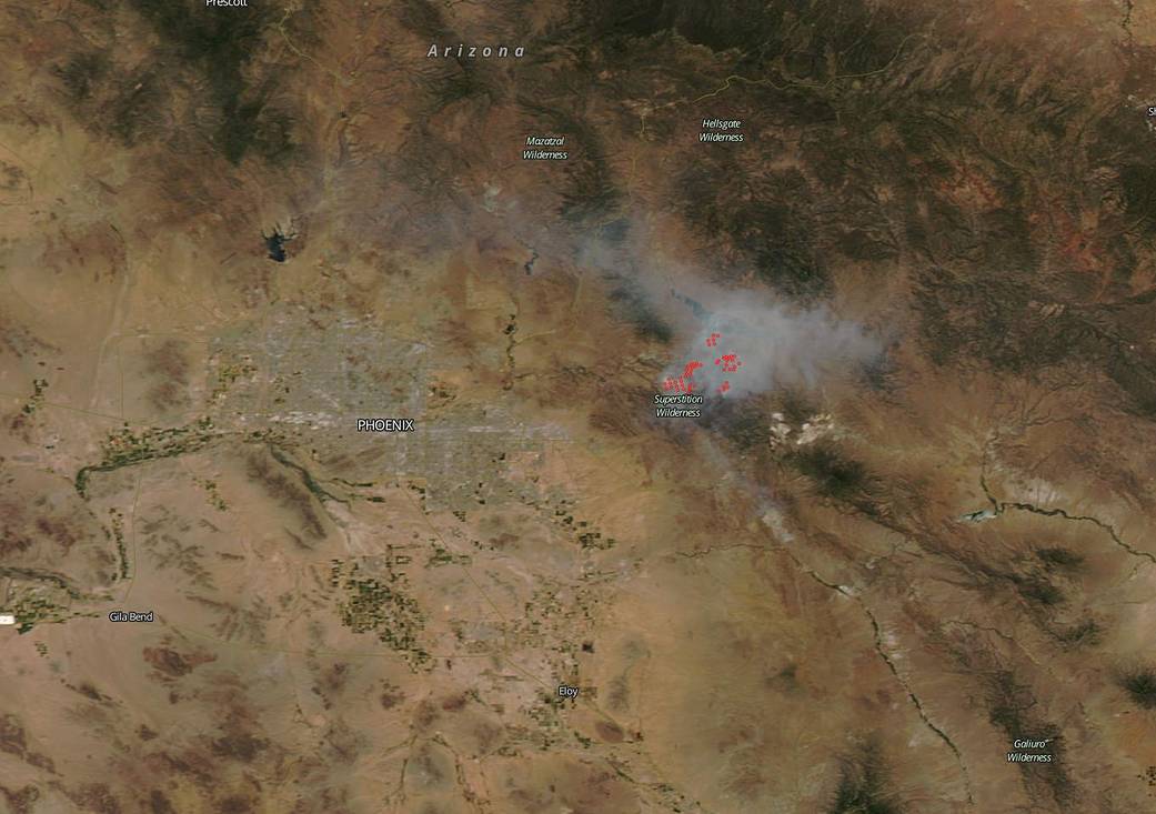 satellite image of land in tan and forest green with puff of smoke