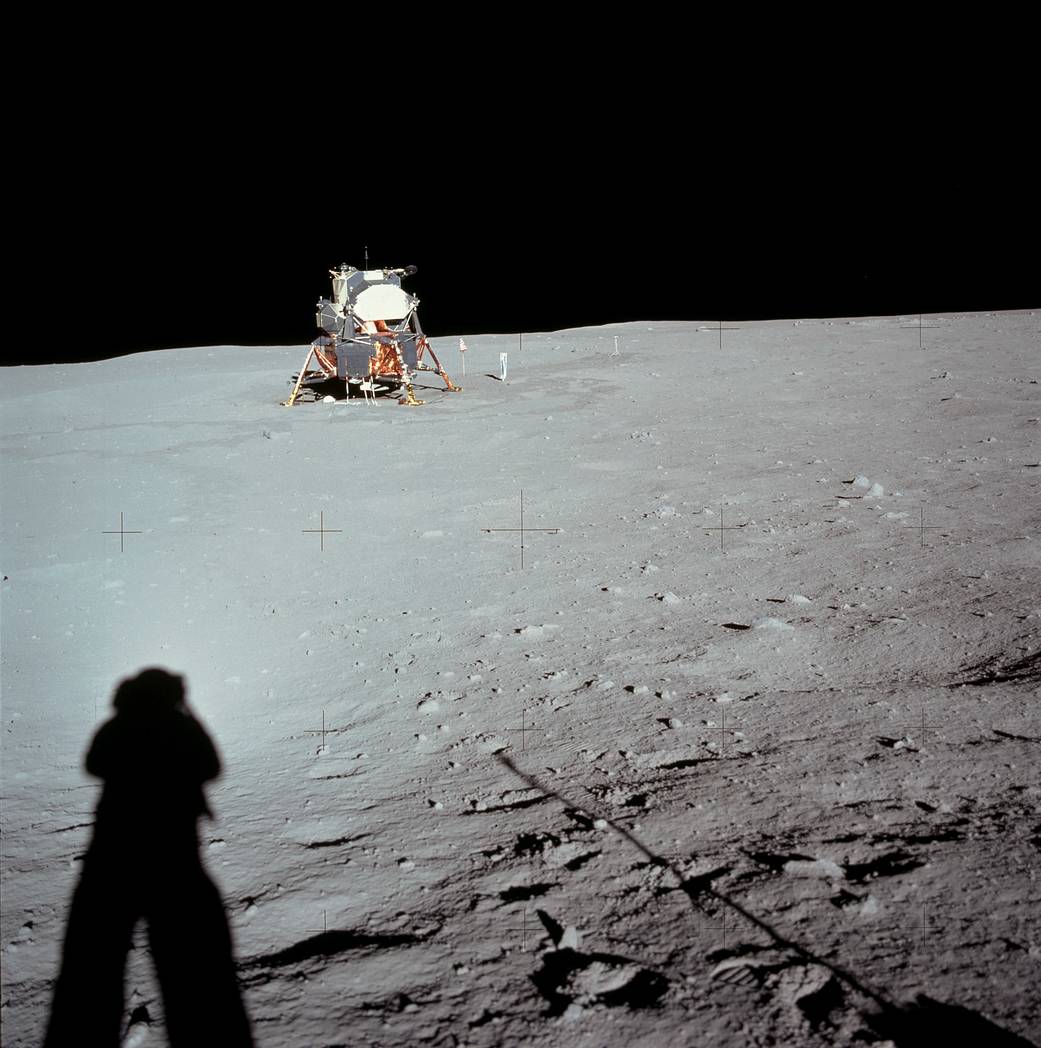 Lunar module on surface of moon with astronaut's shadow in lower left of frame