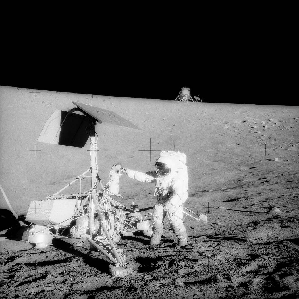 Apollo 12 astronauts visiting Surveyor 3 spacecraft on lunar surface.