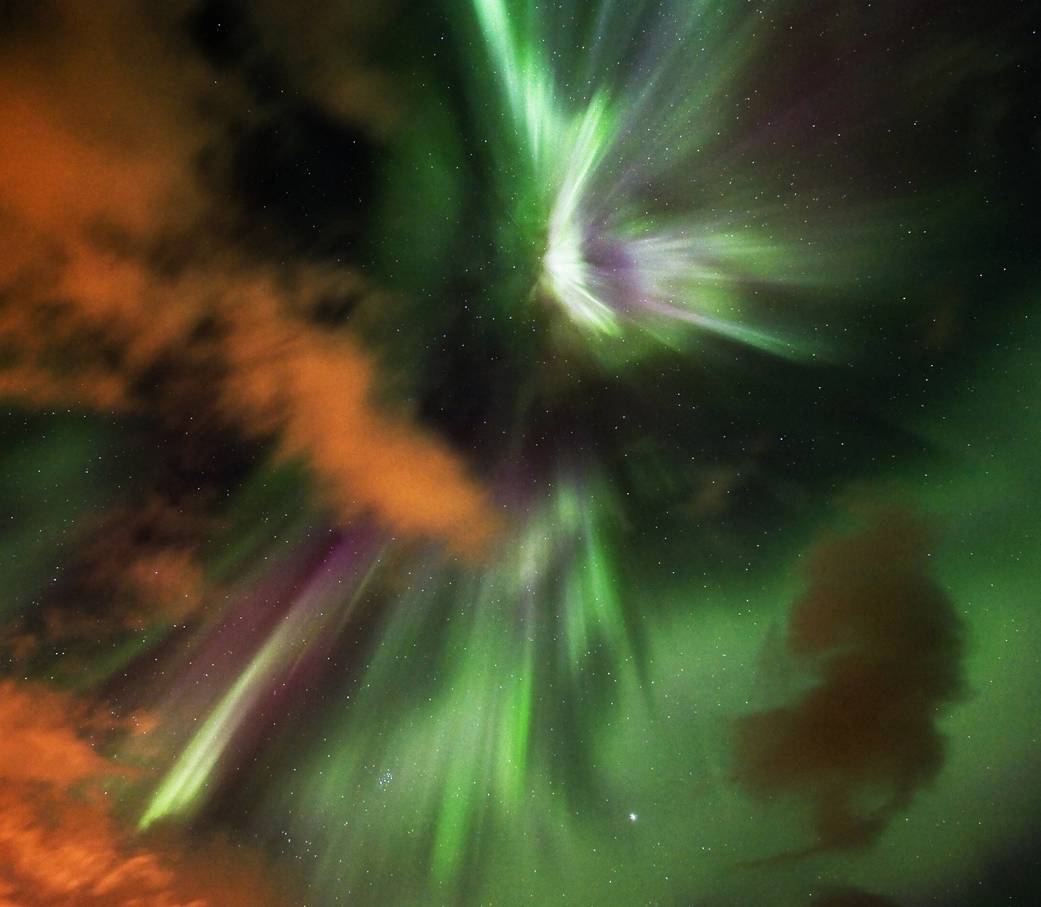 Aurora framed by orange tinted rain clouds.