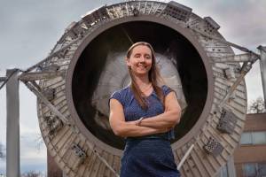 Woman stands with arms folded in front of a rocket display outdoors.