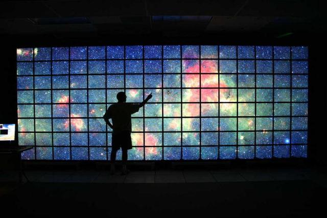 Person in front of Milk Way displayed across many screens