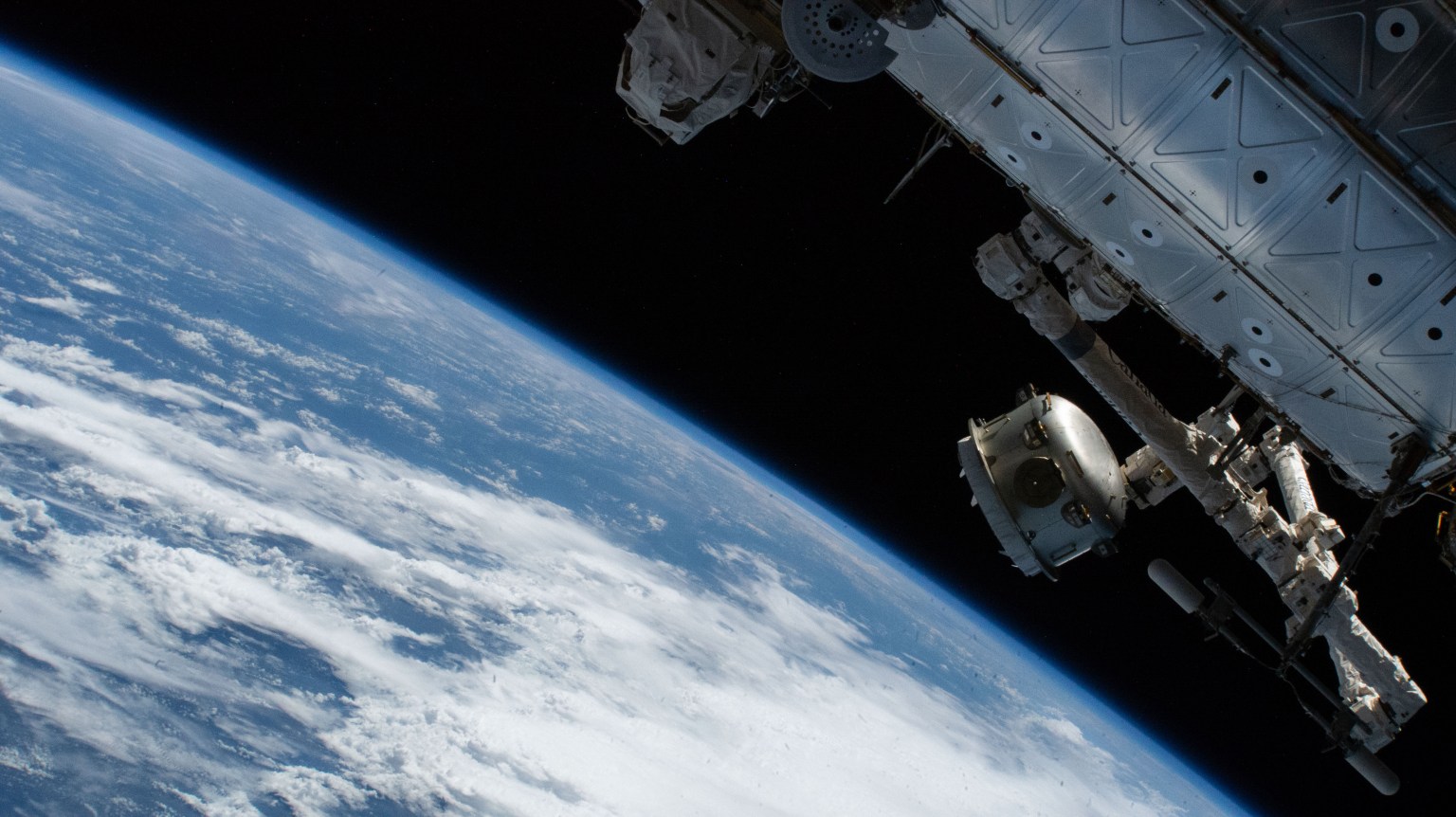 The Nanoracks Bishop Airlock is pictured in the grips of the Canadarm2 robotic arm as it is positioned away from the International Space Station. The commercial platform was being maneuvered prior to jettisoning a trash container for a fiery, but safe disposal above Earth's atmosphere. Bishop is a multi-faceted airlock attached to the Tranquility module used not only to discard trash, but also to host research payloads, deploy satellites, and serve as a testbed for a variety of space technologies. At right, the Canadarm2 is attached to the U.S. Destiny laboratory module as ground controllers remotely maneuver the robotic arm.