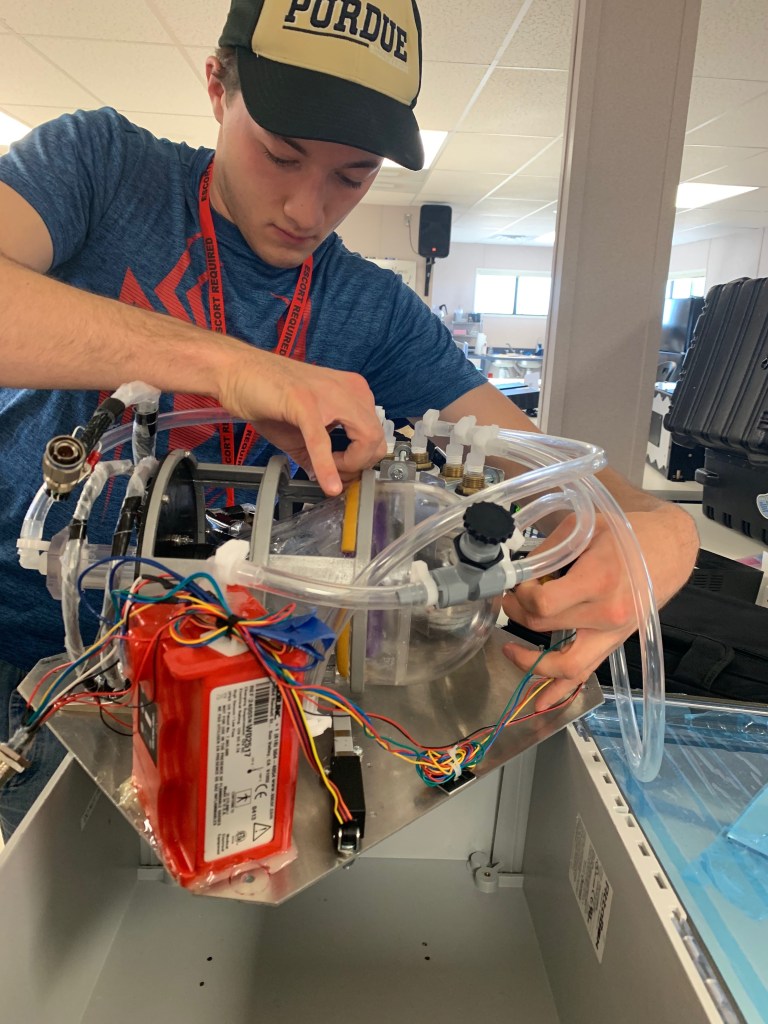 Researcher wearing a Purdue baseball cap handles equipment