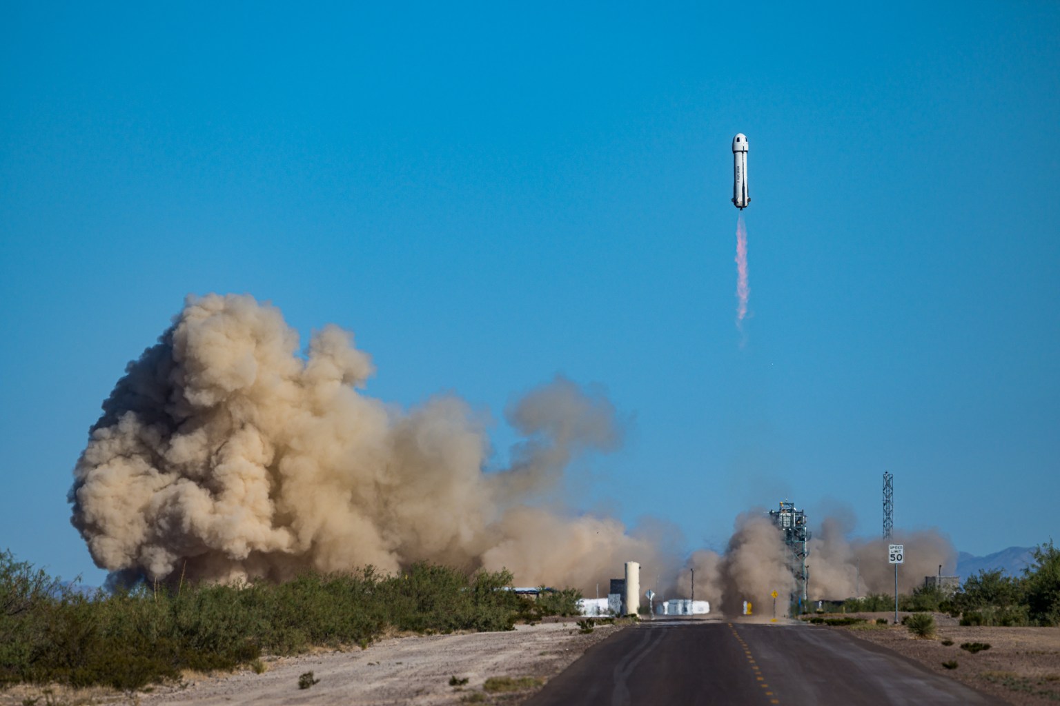 Rocket launches amongst billowing clouds against a blue sky.