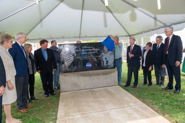 Commemorative marker is unveiled with surrounding dignitaries watching.