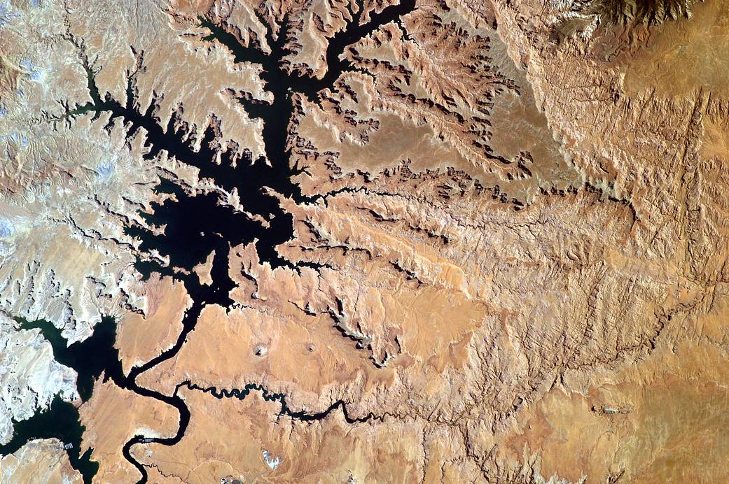 Deep blue reservoir lake and desert landscape photographed from orbit
