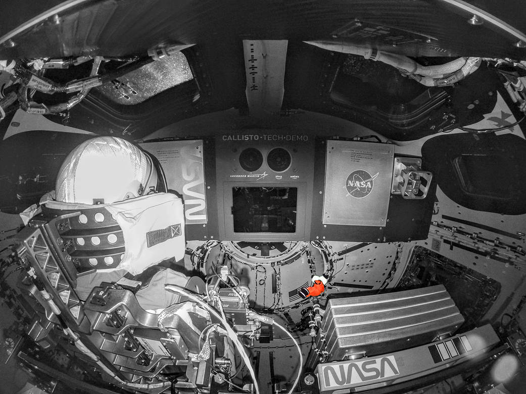 A mostly black and white photo of the interior of the Orion spacecraft. Snoopy, the zero-gravity indicator, is visible in orange.