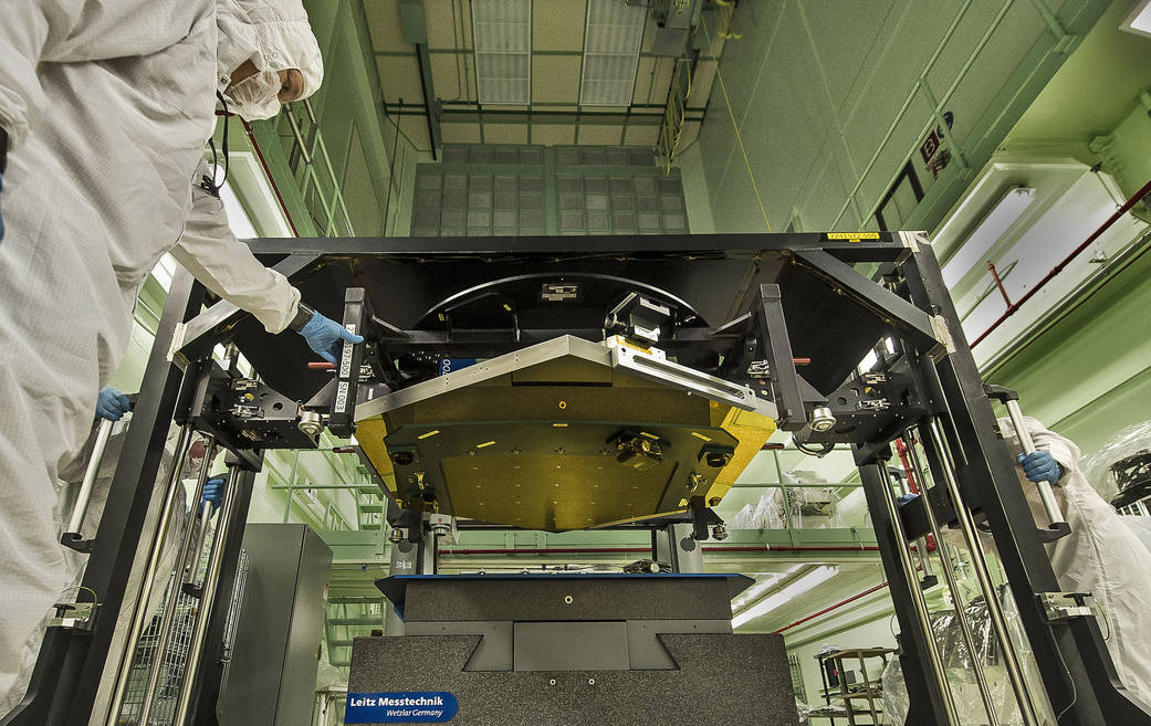 Technicians in clean suits and gloves move rack holding gold hexagonal telescope mirror