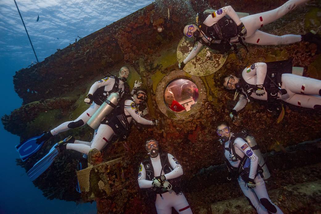 Aquanauts in dive suits pose for photo outside undersea habitat