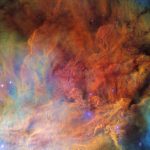 Clouds of gas cover the entire view, in a variety of bold colors. In the center the gas is brighter and very textured, resembling dense smoke. Around the edges it is sparser and fainter. Several small, bright blue stars are scattered over the nebula.
