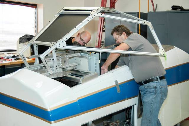 Simulation technicians Brent Bieber, left, and Dennis Pitts install a boilerplate Dream Chaser canopy structure over the cockpit
