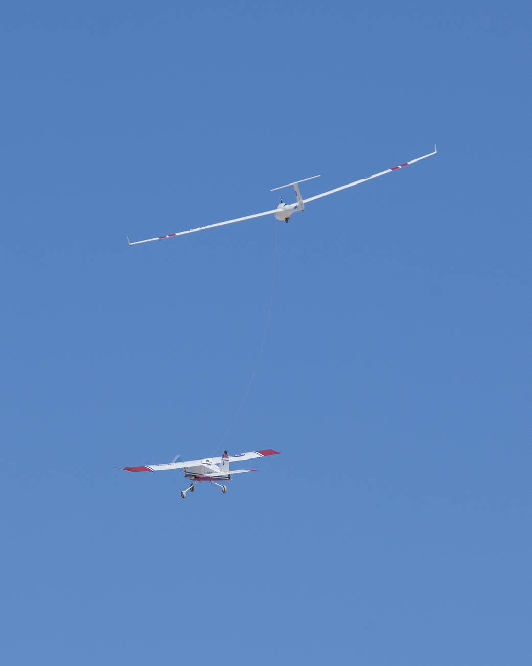 With its towline barely visible against the blue sky, the DROID-3 tow plane hauls a sub-scale sailplane through the air above Ro