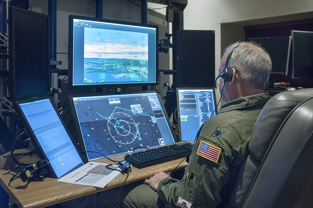 Image of pilot in front of several computer monitors 