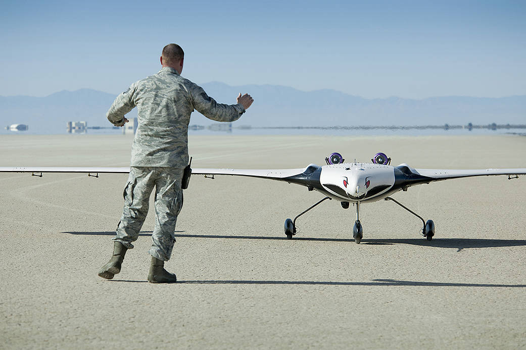 Small white test aircraft with eyes painted on it facing forward, while U.S. Air Force team member in uniform stands to the left