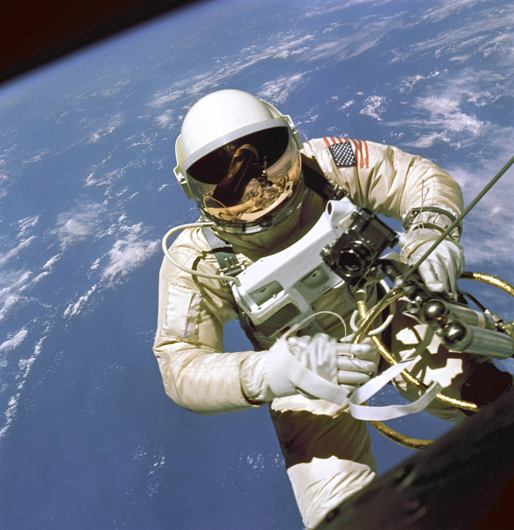 Astronaut Ed White in spacesuit on spacewalk with gold tether cable and Earth visible in background