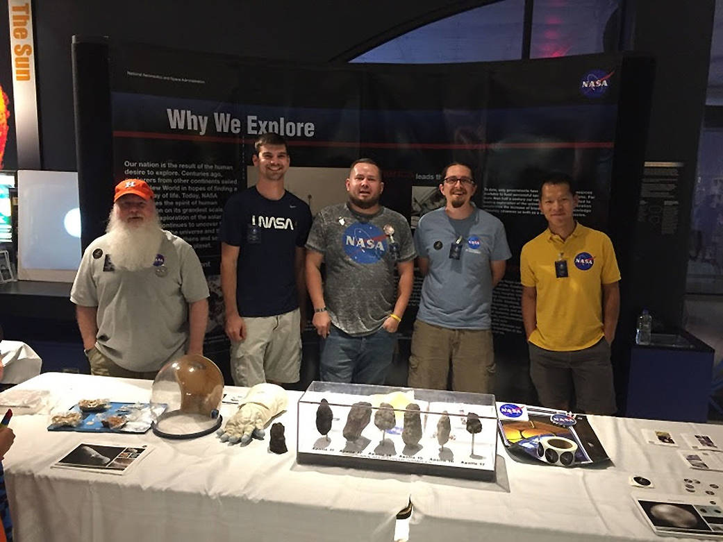 Five men stand in an exhibit booth displaying NASA artifacts